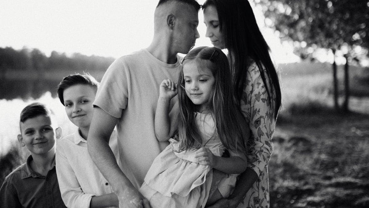 A serene black and white portrait of a family standing by a lake.